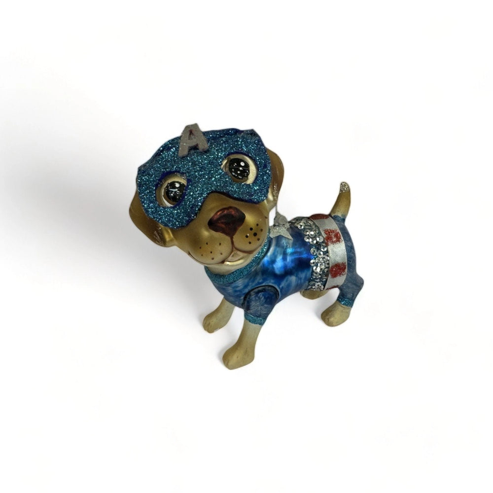 Hand-painted glass Christmas ornament of a puppy wearing a glittering Mister America superhero costume with blue mask and festive details