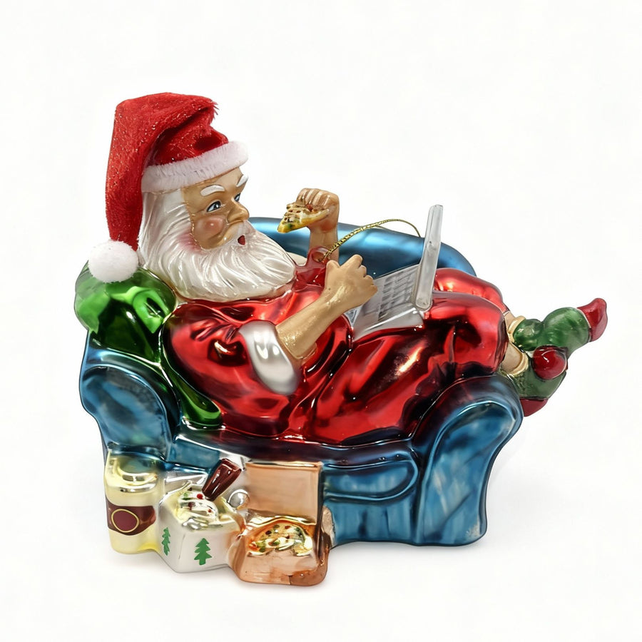 Glass Christmas Santa Claus ornament lounging on sofa with laptop in cozy festive living room, perfect holiday decoration for sale