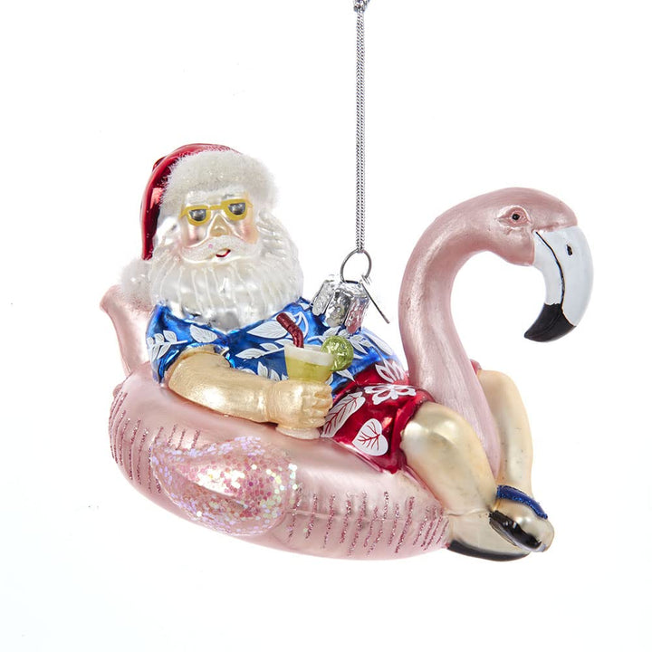 Handcrafted glass ornament of Santa in swimsuit with pink flamingo float